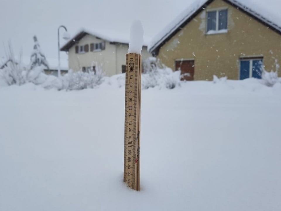 Messstab steckt im Tiefschnee und im Hintergrund ein Haus.