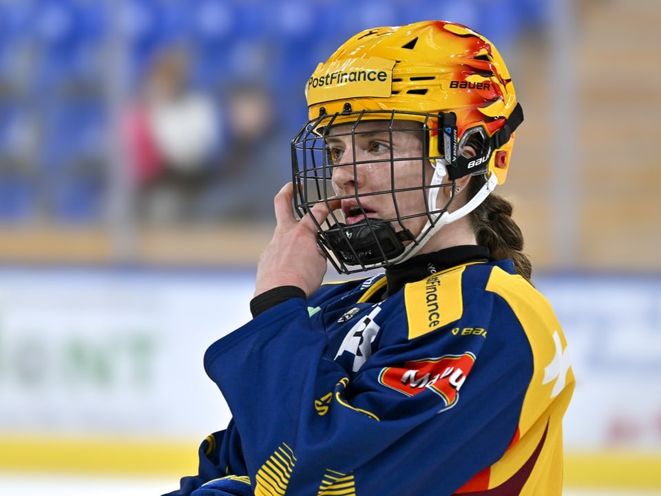 Eishockeyspielerin mit gelbem Helm und blauem Trikot auf dem Eis.