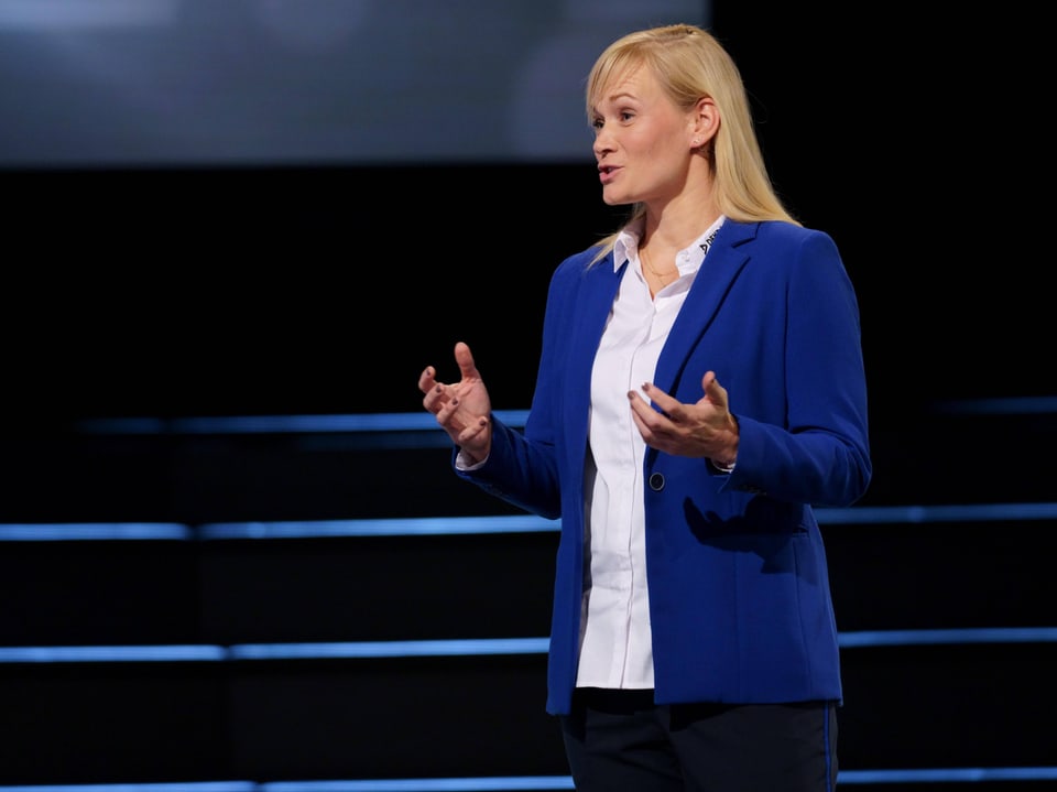 Frau in blauem Blazer hält Vortrag auf Bühne.