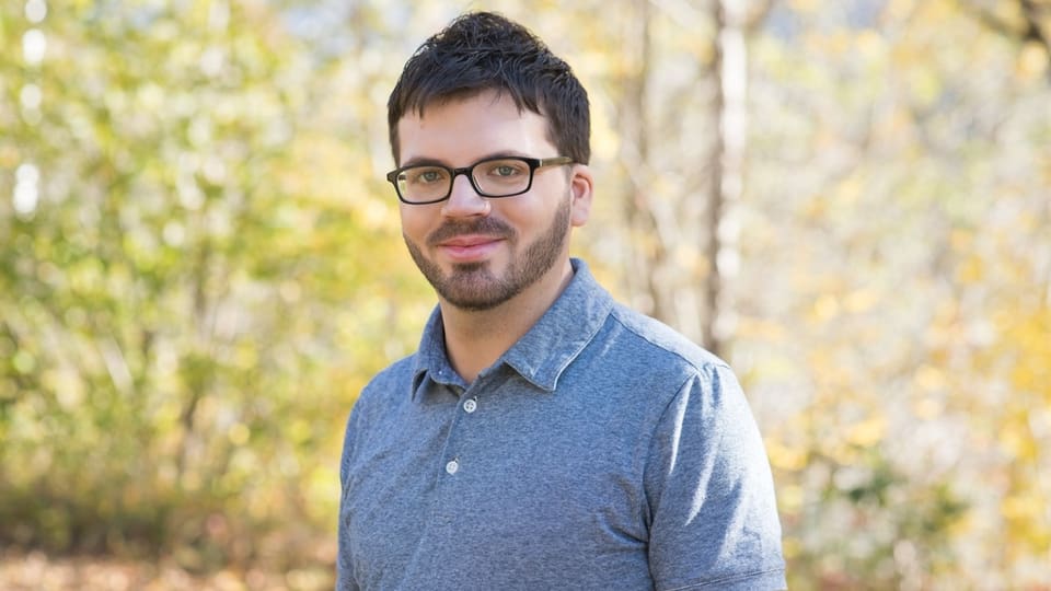 Mann mit Brille im Freien vor unscharfem Hintergrund.