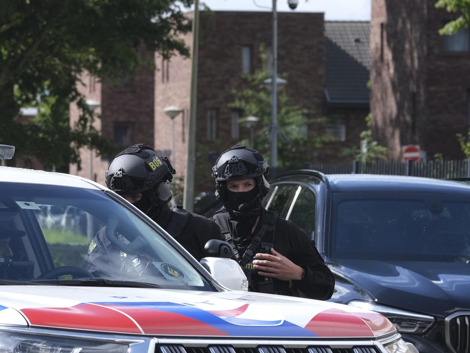 Zwei Sicherheitspolizisten in Schutzkleidung stehen neben einem Polizeifahrzeug.