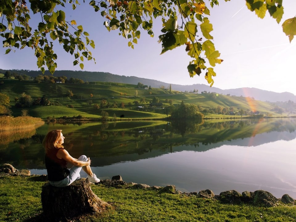 Eine Frau geniesst die wärmende Sonne und die Farben des Herbst am Huettnersee bei Samstagern im Kanton Zürich.