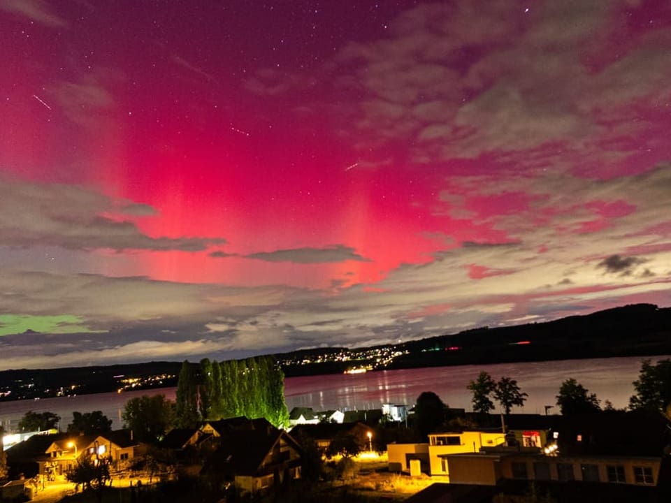 Rotes Nordlicht über Seelandschaft und Häusern.