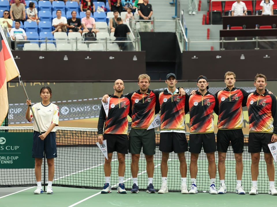 Tennismannschaft mit Deutschlandflagge posiert vor dem Netz auf dem Tennisplatz.