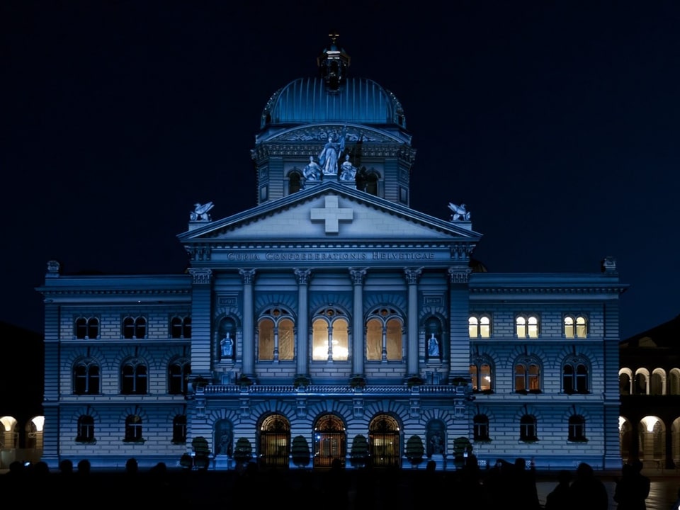 Bundeshaus im Dunkeln mti einem Schweizerkreuz auf der Fassade.