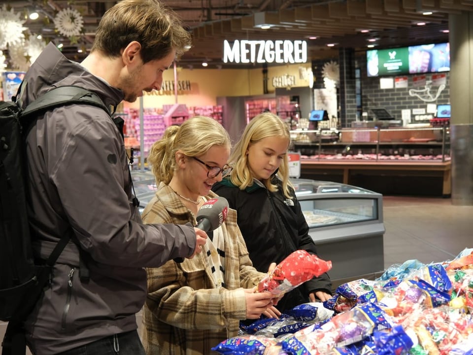 Drei Menschen stehen vor einem grossen Haufen Weihnachtsschokolade. 