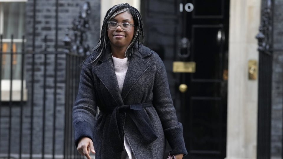 Kemi Badenoch vor der Downing Street in London. Sie trägt einen Mantel, ist eine person of colour, bebrillt, lächelnd.