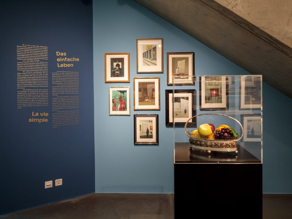 Kunstausstellung mit Fotografien und Obstschale hinter Glas.