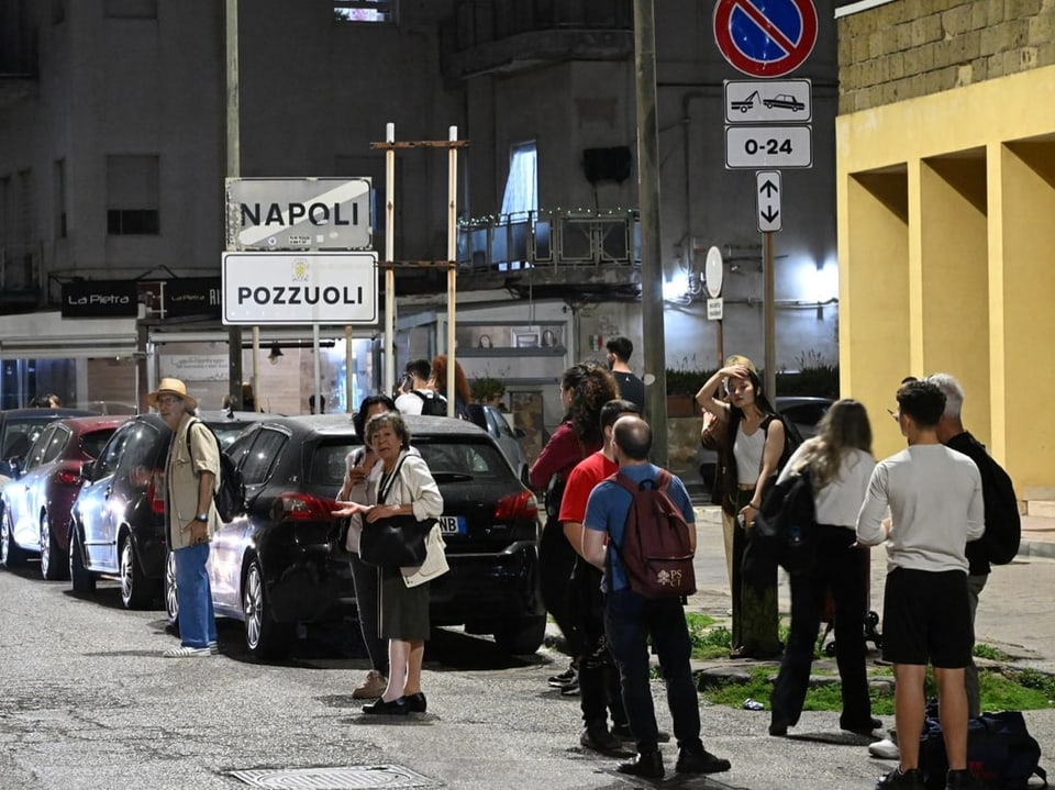 Menschen warten nachts auf der Strasse neben Strassenschildern für Neapel und Pozzuoli.