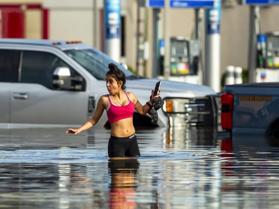 Eine Frau steht im hohen Wasser vor Autos. 