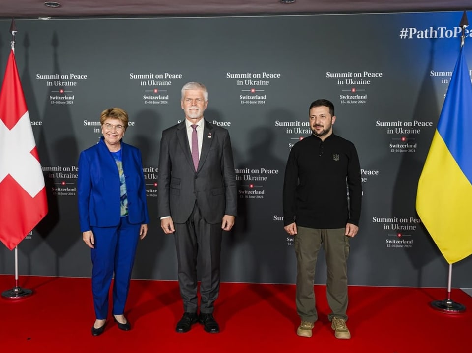 Amherd, Pavel und Selenski vor Bannern bei Friedensgipfel zwischen Schweizer und ukrainischer Flagge.