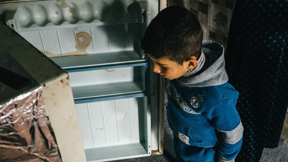 Junge schaut in leeren Kühlschrank.
