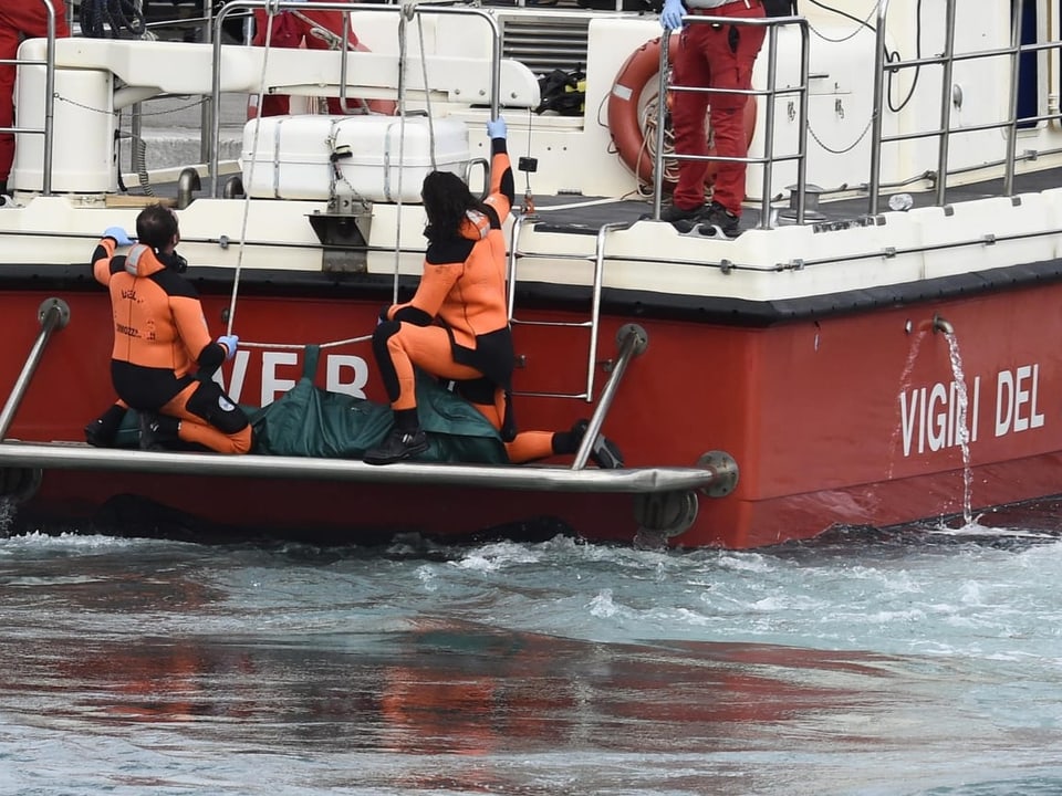 Rettungskräfte bergen Person aus dem Wasser auf einem Boot mit der Aufschrift 'Vigili del Fuoco'.