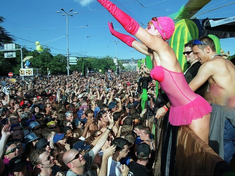 Street Parade, viele Menschen auf Strasse, pink angezogene Frau auf Love Mobile rechts im Bild.