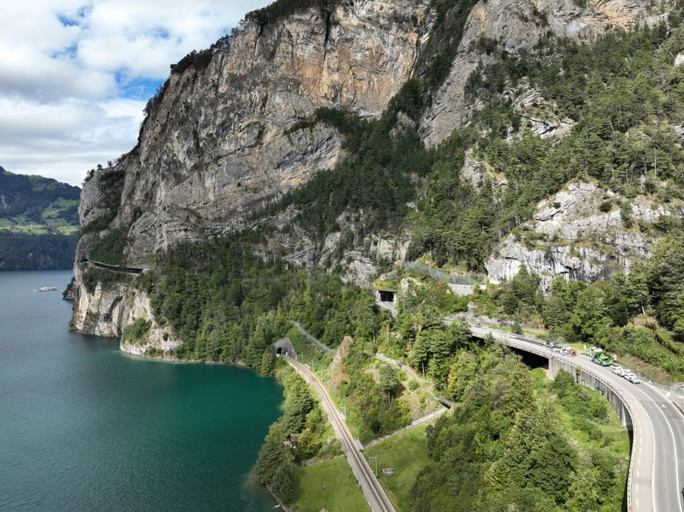 Küstenstrasse und Eisenbahntunnel entlang eines Sees und Felsen.