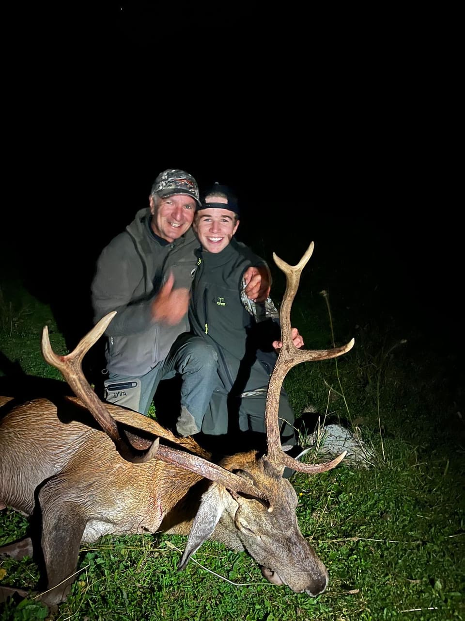 Zwei Jäger posieren nachts mit einem erlegten Hirsch.