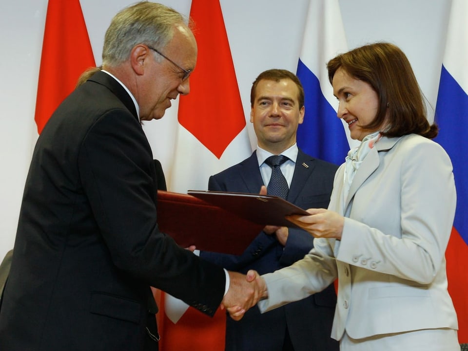 Johann Schneider-Ammann (links) schüttelt Elwira Nabiullina (rechts) die bei einer Dokumentenübergabe die Hand. im Hintergrund steht Dmitri Medwedew.