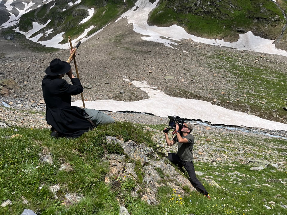 Kameramann fotografiert Person in traditioneller Kleidung in bergiger Landschaft.